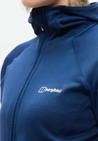 Άτομο που φοράει μπλε μπουφάν Berghaus με φερμουάρ και ψηλό γιακά, δείχνοντας την περιοχή του στήθους και του λαιμού.