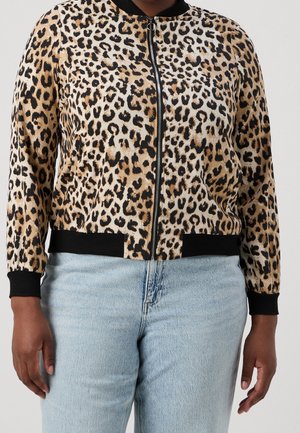 Persoon die een jas met luipaardprint draagt met een zwarte kraag en manchetten, gecombineerd met lichtblauwe spijkerbroek.