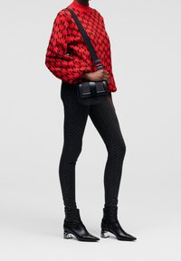 Red sweater with black houndstooth pattern, black textured leggings, and glossy black ankle boots with unique heel design. Small black bag.