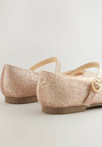 Rozā spīdīgas balerīnas ar noapaļotu formu, regulējamu siksniņu un zelta apaļu sprādzi kā akcentu. Plakana zole un gluda iekšējā oderējums.