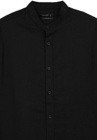 Chemise noire à boutons avec col mao, coupe confortable et tissu texturé. Sept boutons foncés sur le devant.