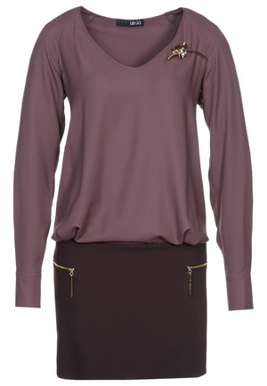 Top a maniche lunghe in tessuto malva con scollatura a V, caratterizzato da una spilla decorativa. La parte inferiore è una gonna marrone con due tasche zippate.