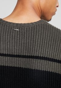 Strickpullover in Dunkelgrau mit schwarzen und hellgrauen Streifen. Verfügt über eine gerippte Textur und ein kleines Metall-Logo-Label am Nacken hinten.