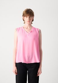 Mouwloze roze blouse met een V-hals ontwerp, lichte textuur en een relaxte pasvorm, gecombineerd met zwarte broek met een stippenpatroon.