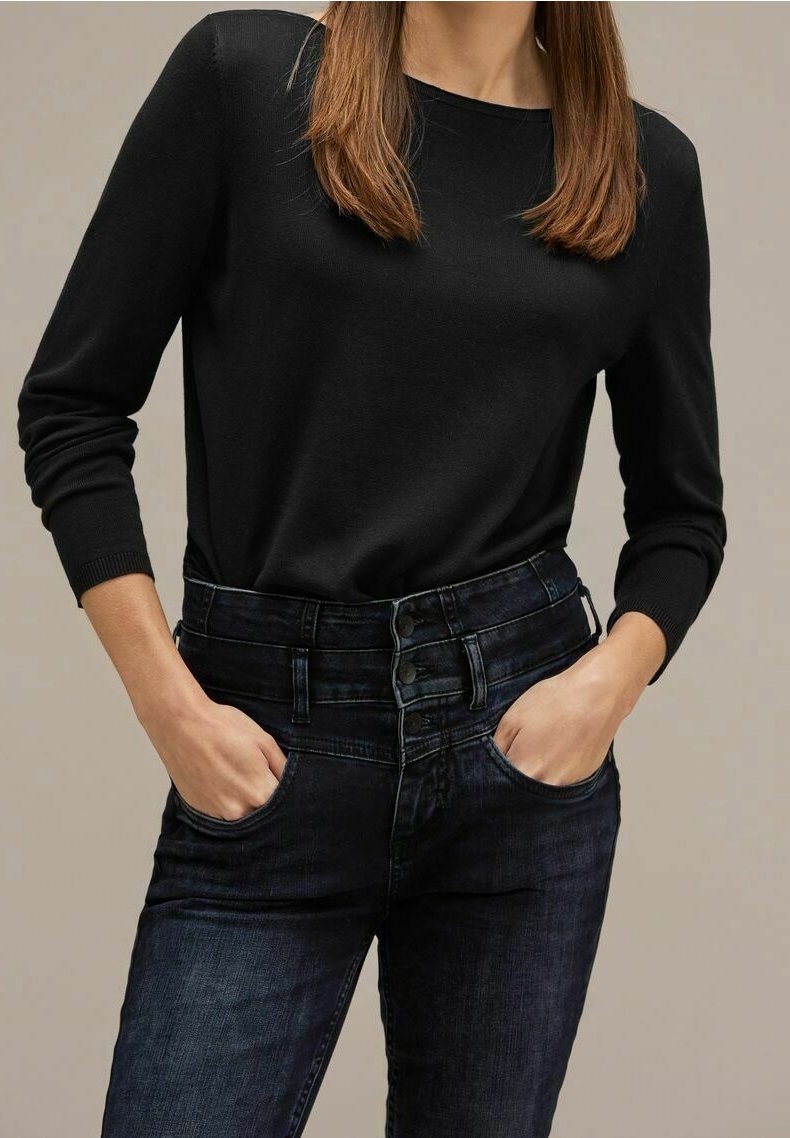 Svart stickad tröja med långa ärmar, kombinerad med mörkblå högmidjade jeans som har knappstängning och sidofickor.