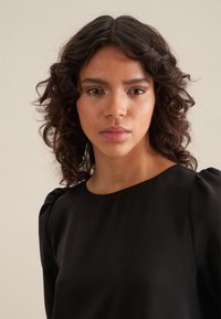 Schwarze Bluse mit rundem Ausschnitt und gepufften kurzen Ärmeln. Glatte Stofftextur, minimalistisches Design ohne sichtbare Muster oder Akzente.