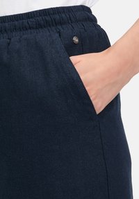 Pantaloni in lino blu navy con vita elastica, che presentano una tasca con dettaglio a bottone a pressione argentato e una superficie liscia.