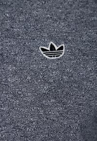 Tmavě modrá texturovaná tkanina s malým bílým logem Adidas, které představuje tři listy. Textura je pletená a vypadá měkce.