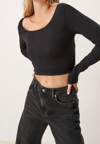 Svart långärmad crop top med en bred rundad halsringning. Kombinerad med högmidjade svarta denimjeans som har en avslappnad passform och en urtvättad textur.