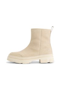 Beige suede enkellaars met dikke gestructureerde zool, ronde neus, trekband aan de achterkant en subtiele reliëf logo aan de zijkant.