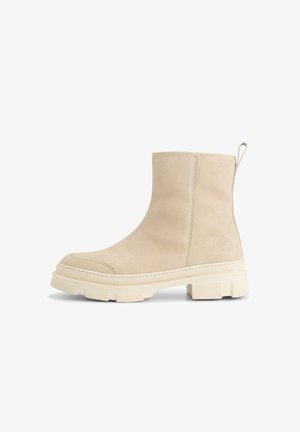 Beige suede ankle boot with thick textured sole, rounded toe, pull tab at the back, and subtle embossed logo on the side.