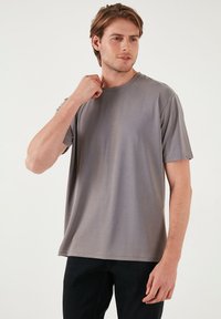 Tricou gri cu mâneci scurte, fabricat dintr-un material neted, având decolteu rotund și o croială lejeră. Design simplu, fără modele sau accente.