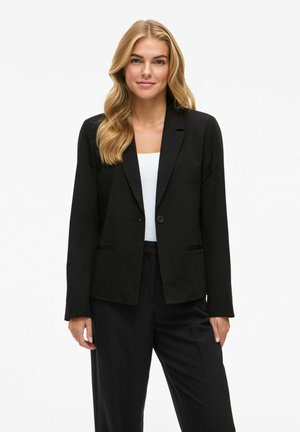 Blazer nero con chiusura a un bottone, rever a lancia e due tasche frontali; abbinato a una maglietta bianca e pantaloni neri. Texture liscia.