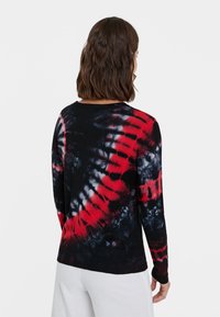 Pull à manches longues avec un motif tie-dye en noir, rouge et blanc, fabriqué dans un tissu texturé avec un col rond.
