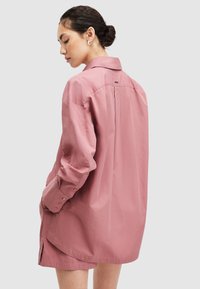 Camisa rosa de gran tamaño en tejido ligero con cuello, puños abotonados y aberturas laterales, que presenta un diseño sencillo y un corte relajado.