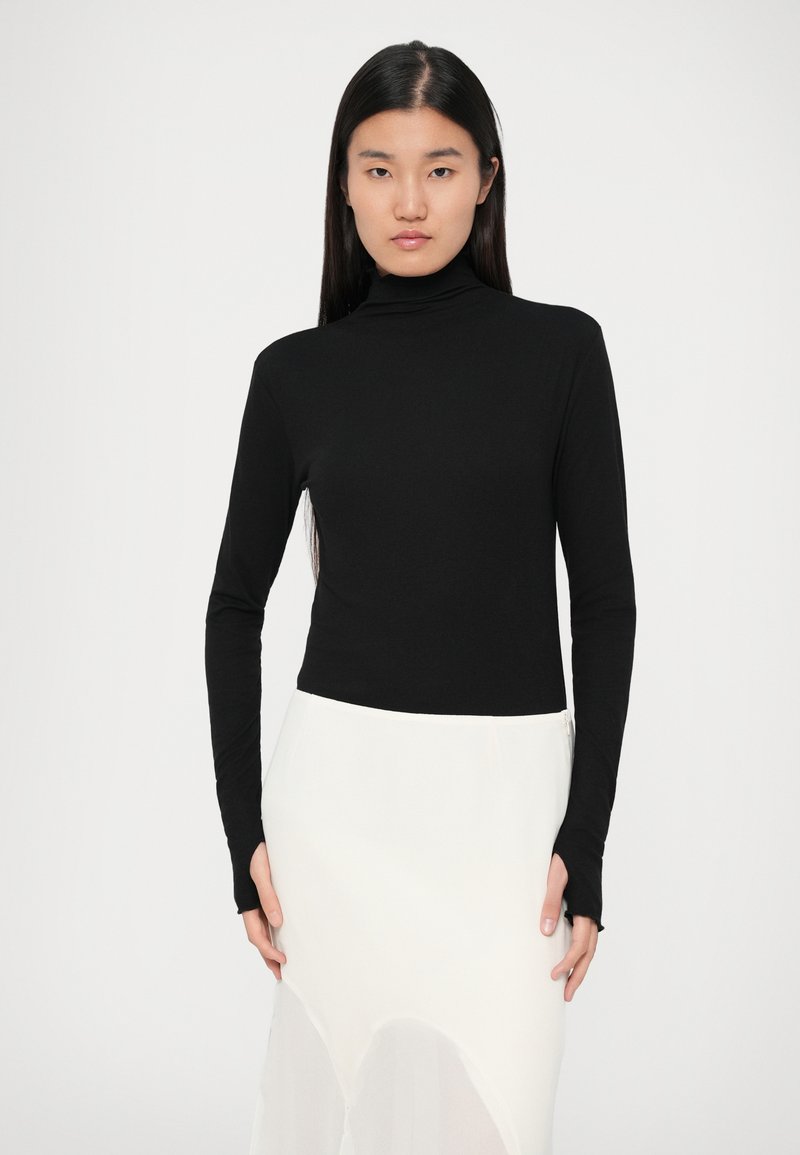 Schwarzes langärmliges Turtleneck-Oberteil in figurbetonter Passform, aus glattem Stoff gefertigt. Kombiniert mit einem weißen, durchsichtigen Rock mit abgerundetem Saum.