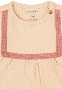 Licht perzik katoen top met een textuur ribbelpatroon, voorzien van een roze gebreide rand, knoopsluiting en geplooide details bij de taille.