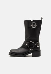 Stivale alla caviglia in pelle nera con punta rotonda, accessori in argento, due fibbie, una cinghia con anello metallico e tacco spesso.