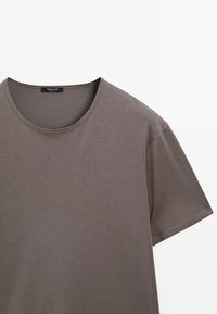 Světle šedé triko s krátkým rukávem z hladké, lehké látky, s kulatým výstřihem a švem podél okrajů.