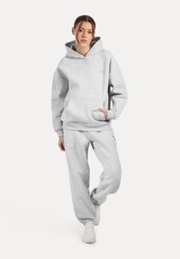 Grijze sweatshirt en bijpassende trainingsbroek van een katoenmix. De hoodie heeft een voorzak; de outfit heeft een relaxte pasvorm. Witte sneakers.