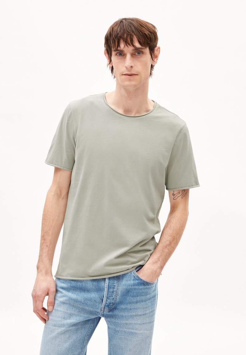 Helles grünes T-Shirt mit kurzen Ärmeln aus weichem Stoff und rundem Ausschnitt, kombiniert mit hellblauen Denim-Jeans, die eine dezente Waschwirkung aufweisen.