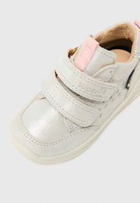 Lys grå sneaker med metallisk finish, doble borrelåser, rosa detaljer og teksturert interiør. Rund tå og hvit såle.