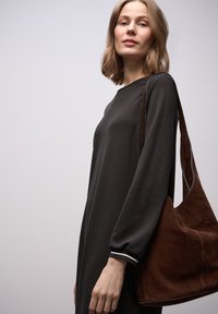 Pitkähihaiset, tummanharmaat mekot, joissa on rento istuvuus, pyöreä pääntie ja raidalliset kalvosimet. Henkilöllä on myös ruskea mokkanahkainen olkalaukku.