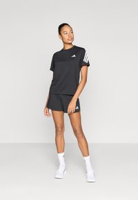 Czarna sportowa koszulka z okrągłym dekoltem, z trzema białymi paskami na lewym ramieniu, w komplecie z dopasowanymi czarnymi szortami.