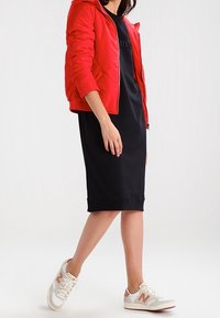 Rode pufferjas met ritssluiting, zwart midi-jurkje en witte sneakers met beige accenten. Glad textuur en een aansluitende pasvorm voor casual gebruik.