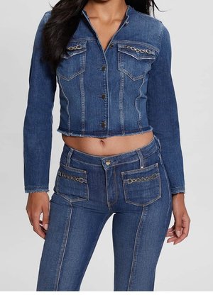 Kvinde iført en tætsiddende, cropped blå denimjakke med guldkædedetaljer og matchende højtaljede denimjeans med forlommer.