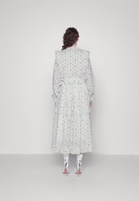 Valkoinen kukkamekko, jossa on kerroksellisia röyhelöitä, pitkät hihat ja korkea kaulus. Yhdistettynä hopeisiin korkokenkiin ja nilkkasukkia.