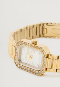 Guldfarvet metal armbåndsur med octagonal kasse, hvid urskive, gulde timermarkeringer og rhinsten aksenter rundt om bezel. Link armbånd design.