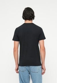 Tricou negru cu mânecă scurtă, de tip crew neckline, design simplu, realizat din bumbac moale, textură netedă, purtat cu blugi albaștri.