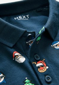 Mörkblå polo skjorta med en texturerad krage, prydd med färgglada julmotiv, knappar och vävd etikett.