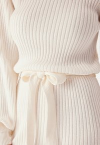 Maglione bianco a costine con maniche lunghe e una cintura a cravatta in vita, che presenta un motivo testurizzato e una vestibilità aderente.