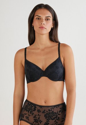 Zwarte kant-bh met bloemenpatroon, gevoerde cups, verstelbare bandjes en gegolfde rand. Gecombineerd met doorschijnende, met bloemen geborduurde, high-waisted slipjes.