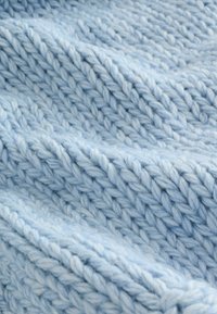 Tissu tricoté bleu clair avec une apparence douce et texturée ; présente un fil épais et des motifs de points visibles, créant un aspect chaleureux.
