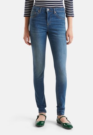 Jeans blu skinny con una finitura sbiadita, cinque tasche, chiusura con bottone e zip, abbinati a scarpe piatte verdi. Tessuto di denim in cotone.
