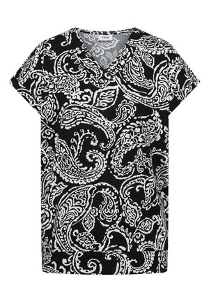 Femme portant un haut à motifs noir et blanc, un jean bleu à jambes larges, des baskets blanches et un grand cabas matelassé vert clair.