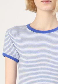 T-shirt rayé en bleu clair et blanc, avec un col rond et des manches courtes, doté de bords côtelés bleus contrastants. Tissu texturé.