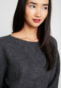 Pull gris à manches longues avec un motif de tricot texturé et un col large et arrondi. Tissu doux avec une coupe légèrement large.