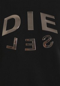 Letras plateadas brillantes que deletrean "DIESEL" con la fila inferior invertida sobre un fondo de tela texturizada negra.