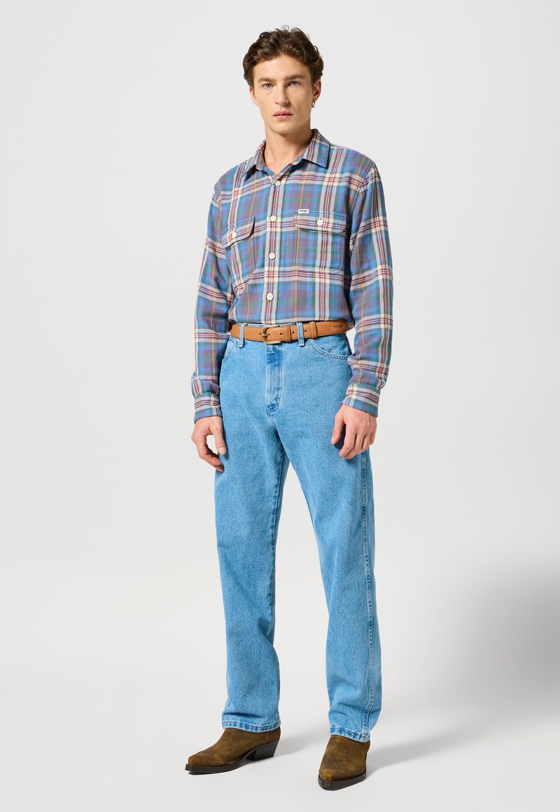 Geruite shirt in tinten blauw, paars en rood; lichtblauwe denim jeans; bruine leren riem; bruine enkellaarsjes; casual fit.