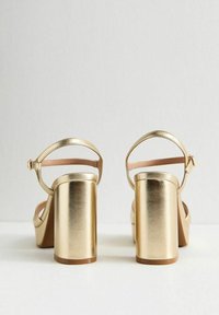 Guldmetalliska plattformssandaler med bred klack och ankelrem. Slät yta med en minimalistisk design. Mjuk rosa innerfoder.