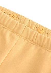 Justerbar elastisk talje med beige stof og matchende knapper til tilpasning af størrelsen på tøjet.
