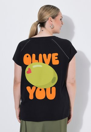 Donna con capelli biondi raccolti in una coda di cavallo che indossa una t-shirt nera con una grande oliva verde e testo arancione "OLIVE YOU" sulla schiena.