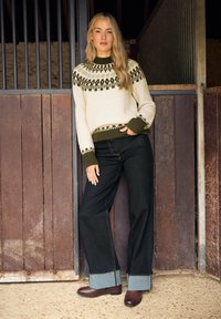 Kermansweater med gröna geometriska mönster, ribbade manschetter, parat med mörka jeans med uppvikta fållar och bruna ankelstövlar.