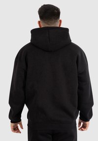Felpa nera con cappuccio caratterizzata da una vestibilità comoda, polsini a costine e una superficie texturizzata. Il design è privo di decorazioni, senza loghi o motivi visibili.