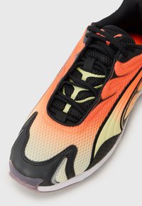 Sneaker de sport avec une tige en mesh en dégradé allant de l'orange au jaune, des accents noirs et des détails texturés. Présente un design de lacets complexe et une semelle en caoutchouc.