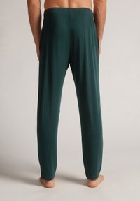 Groene lange broek met een elastische tailleband, gemaakt van een zachte, lichte stof. Heeft een rechte snit en geen zichtbare zakken.